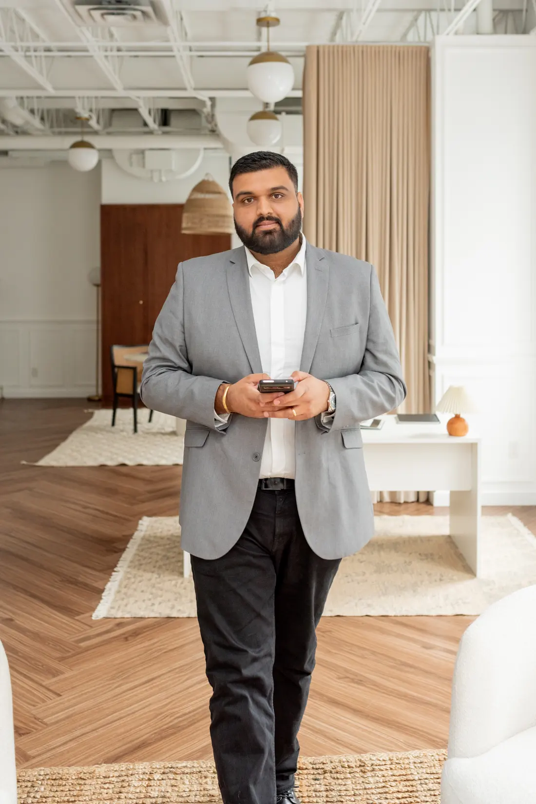 Puneet Mann in a grey blazer, walking through the office with his phone in hand